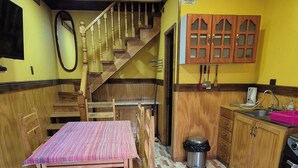 A kitchen with wooden cabinets, a dining table with chairs, a staircase, and a tiled floor. - Cabaña Galvarino Puerto Natales (Natales)