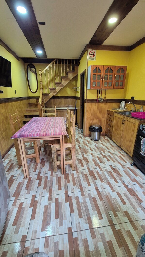 A kitchen with wooden cabinets, a dining table with chairs, a staircase, and a tiled floor.