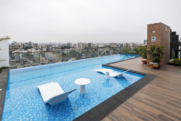 A rooftop infinity pool with lounge chairs and a city view.