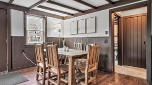 Un comedor con una mesa y sillas de madera, una lámpara y cuadros en la pared.