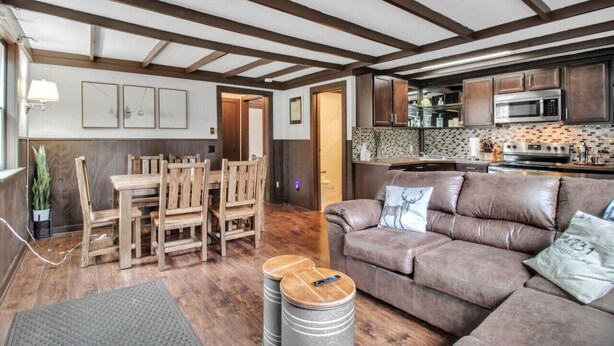 Una sala de estar acogedora con un sofá de cuero marrón, una mesa de comedor de madera y sillas. Hay una zona de cocina con armarios de madera y un microondas.
