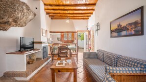 A living room with a television, a wooden table, a sofa, and a painting on the wall. - Holiday Home 'Casa Rural La Roca' with Mountain Views, Shared Pool and Wi-Fi (La Zubia)