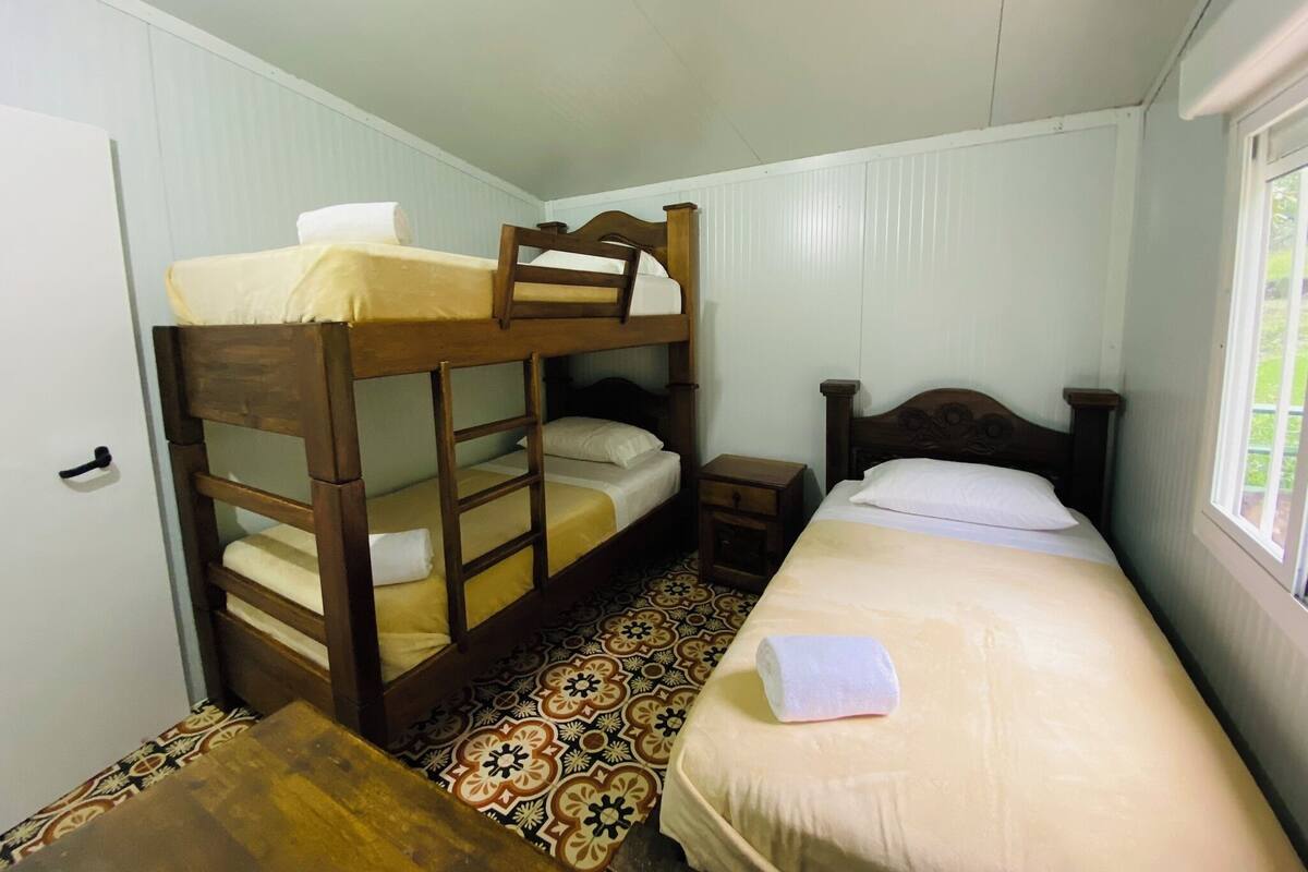 A bunk bed with a wooden headboard, a single bed with a wooden headboard, a small bedside table, and a patterned floor.