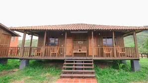 Eine Holzhütte mit Veranda, Stufen, die zum Eingang führen, und Blick ins umliegende Grün.