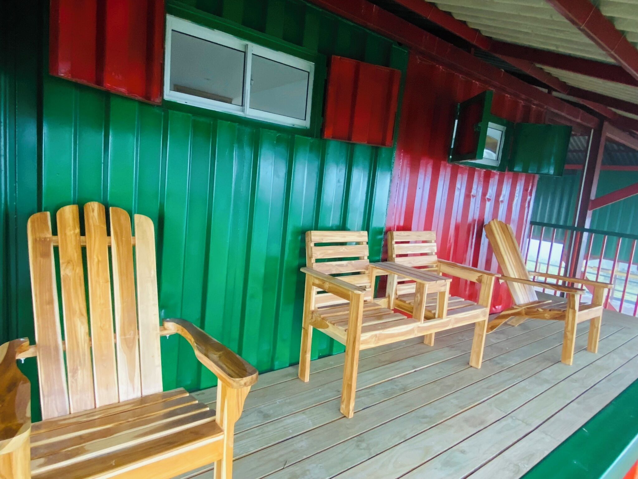 A wooden deck with a green and red wall, featuring two wooden chairs and a small table.