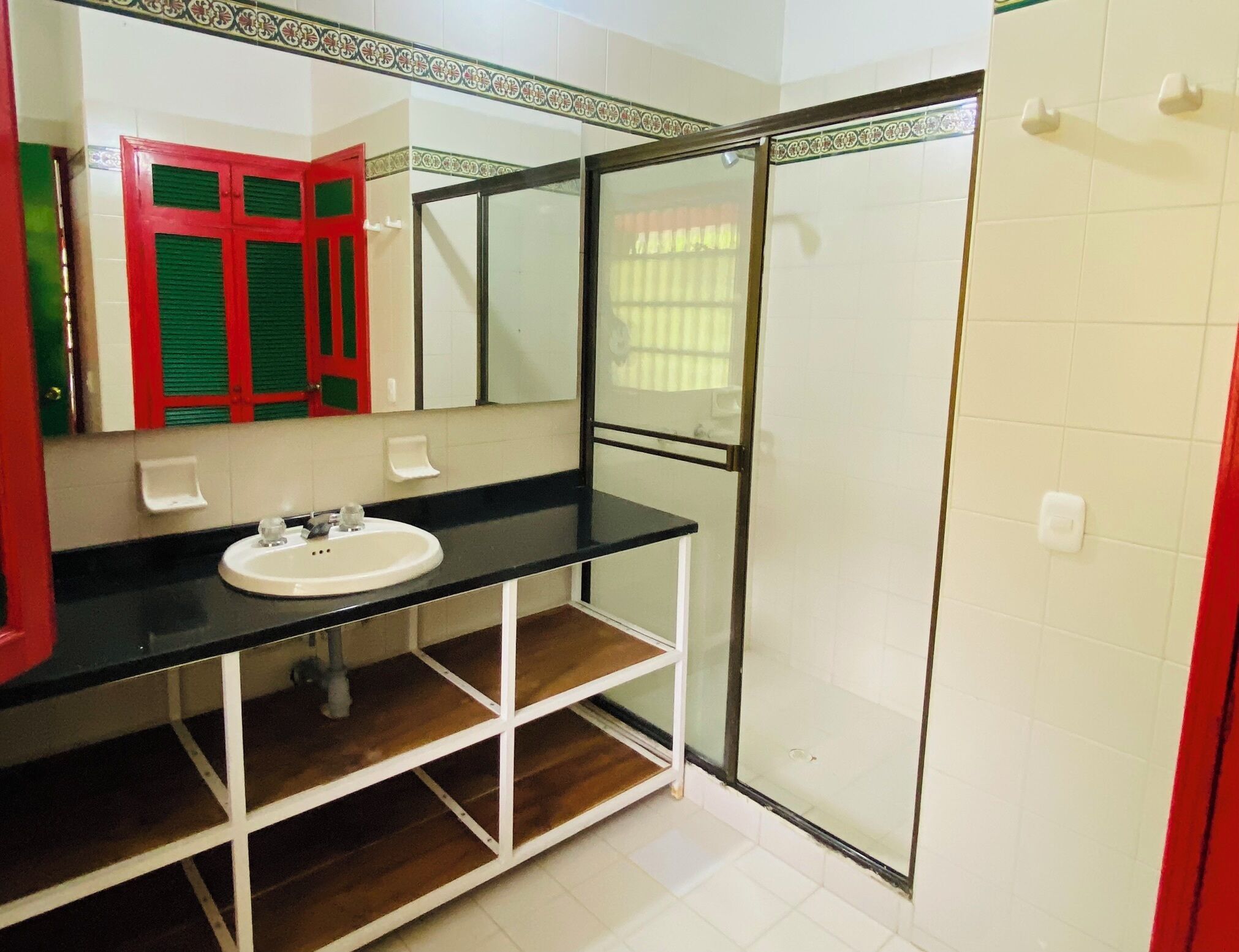 Un baño con lavamanos blanco, espejo, armario rojo y cabina de ducha con paredes de vidrio.