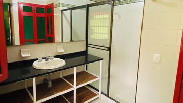 Un baño con lavamanos blanco, espejo, armario rojo y cabina de ducha con paredes de vidrio.