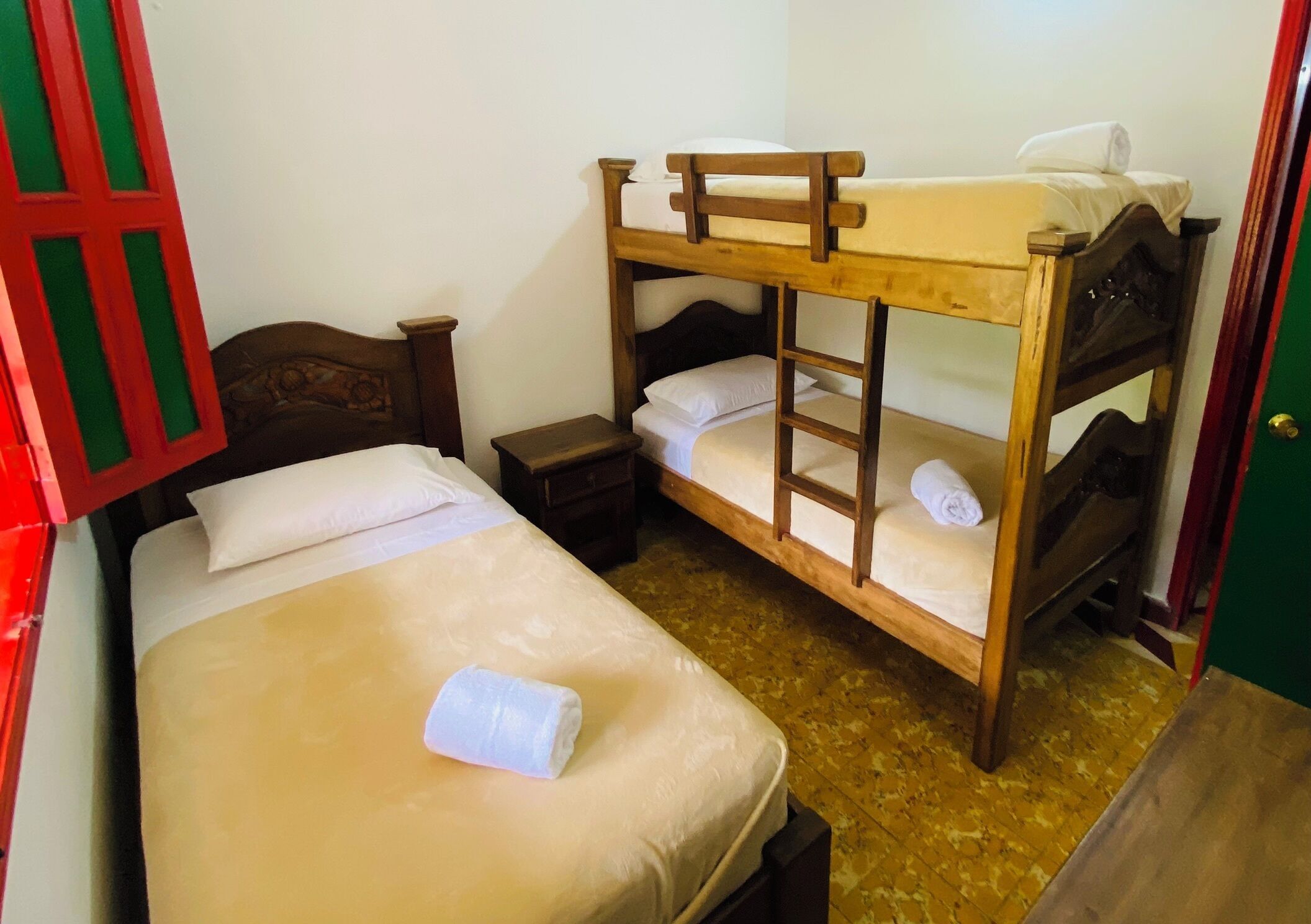 A bunk bed room with a wooden headboard, a small bedside table, and a neatly made bed with a white pillow and a rolled towel.