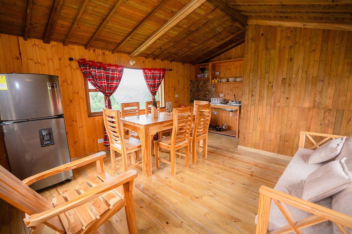 A wooden cabin interior with a dining area, kitchen, and a bed.