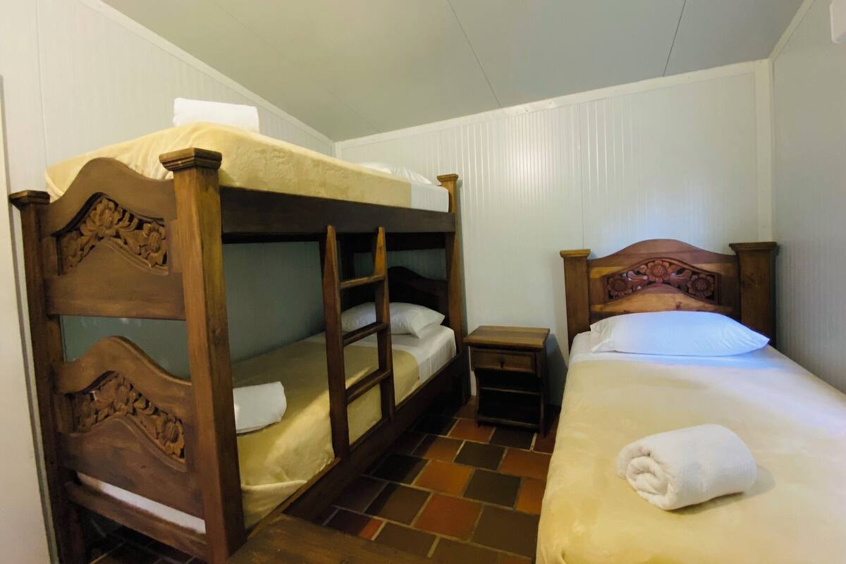 A room with a bunk bed, a single bed, a nightstand, and a tiled floor.