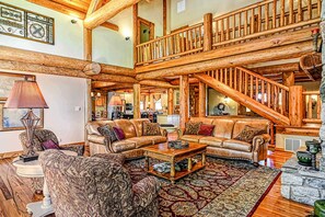 A spacious living area with a high wooden ceiling, a staircase, and a fireplace.