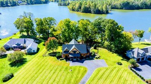 A large house with a steeply pitched roof, surrounded by a well-maintained lawn and a lake.