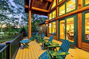 A wooden deck with green Adirondack chairs and a table, overlooking a forested area.