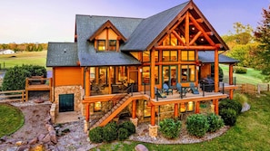 A large log cabin with a stone foundation, multiple decks, and a well-maintained lawn.
