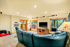 Lower Level Family Room - Dark green leather sectional faces a large TV with lake-themed decor and French doors opening to the patio.