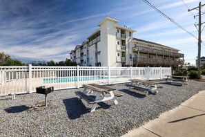 A multi-story building with a pool area, picnic tables, and a white fence. - Ocean and Sound Views at "Shoreline Escape"! (Surf City)
