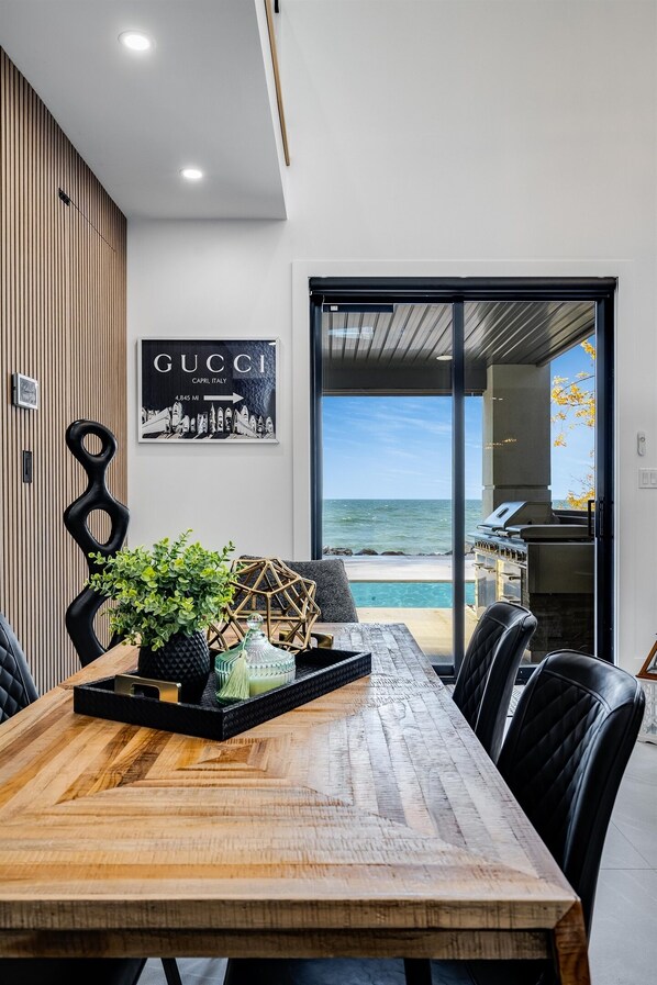 A dining area with a wooden table, black chairs, and a view of the ocean.