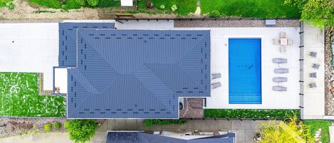 An aerial view of a residential property with a swimming pool, patio furniture, and a well-maintained lawn.