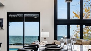 A modern dining area with a long table, black chairs, and a view of the ocean through large windows.