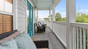 Eine überdachte Veranda mit weißer Reling, einer türkisblauen Tür und Gartenmöbeln, darunter eine Couch und Stühle.