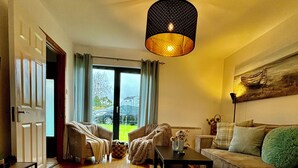 A cozy living room with a wooden floor, a sofa, a coffee table, and a hanging light fixture.