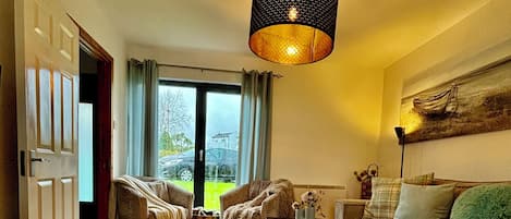 A cozy living room with a wooden floor, a sofa, a coffee table, and a hanging light fixture.