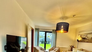 A spacious living room with a wooden floor, a sofa, a chair, a TV, and a dining table.