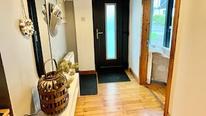 A hallway with wooden flooring, a white bench, a mirror, and a door leading to an outdoor area.