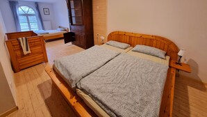 A bedroom with a wooden bed, a wooden wardrobe, a small wooden bench, and a window with curtains. - Vacation apartment Wiesenblick in the Michelshof (Kevelaer)