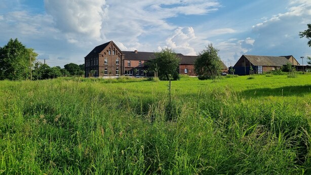 A large, two-story brick building with a gabled roof, surrounded by a lush green field and trees. - Vacation apartment Wiesenblick in the Michelshof (Kevelaer)