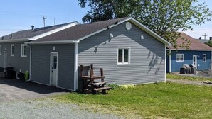 A single-story cabin with a garage, a small porch, and a view of a lake. - SpringHouse Cozy Oceanview 1-Bedroom Apartment Pet-friendly (Lewisporte)