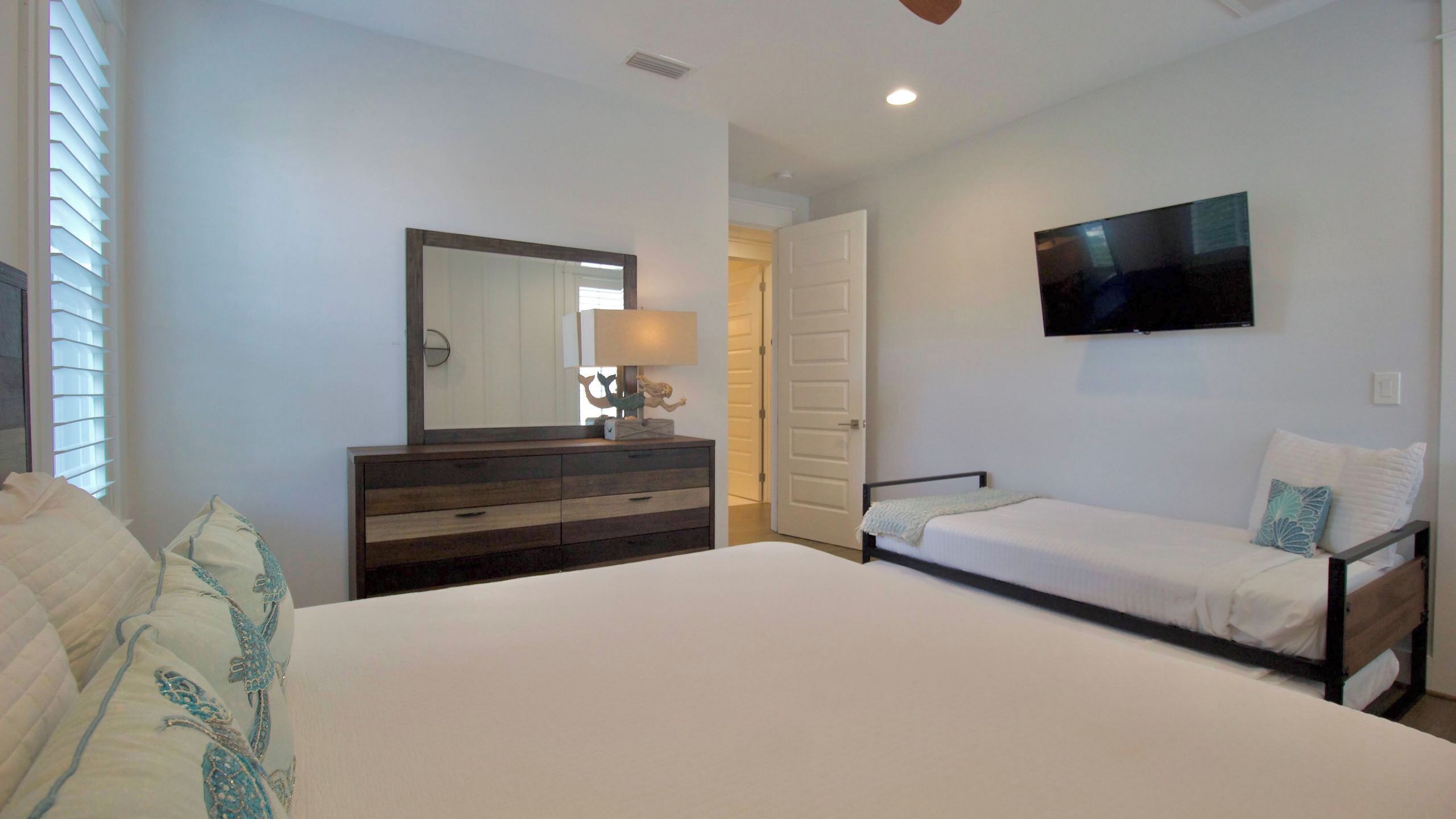 A bedroom with a bed, a dresser, a mirror, a television, and a door.