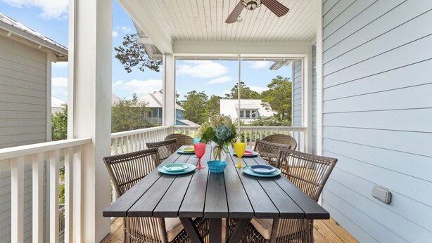 A covered outdoor dining area with a wooden table and wicker chairs, a ceiling fan, and a view of neighboring houses. - Beach Still My Heart by Avantstay with Pool Access (Santa Rosa Beach)