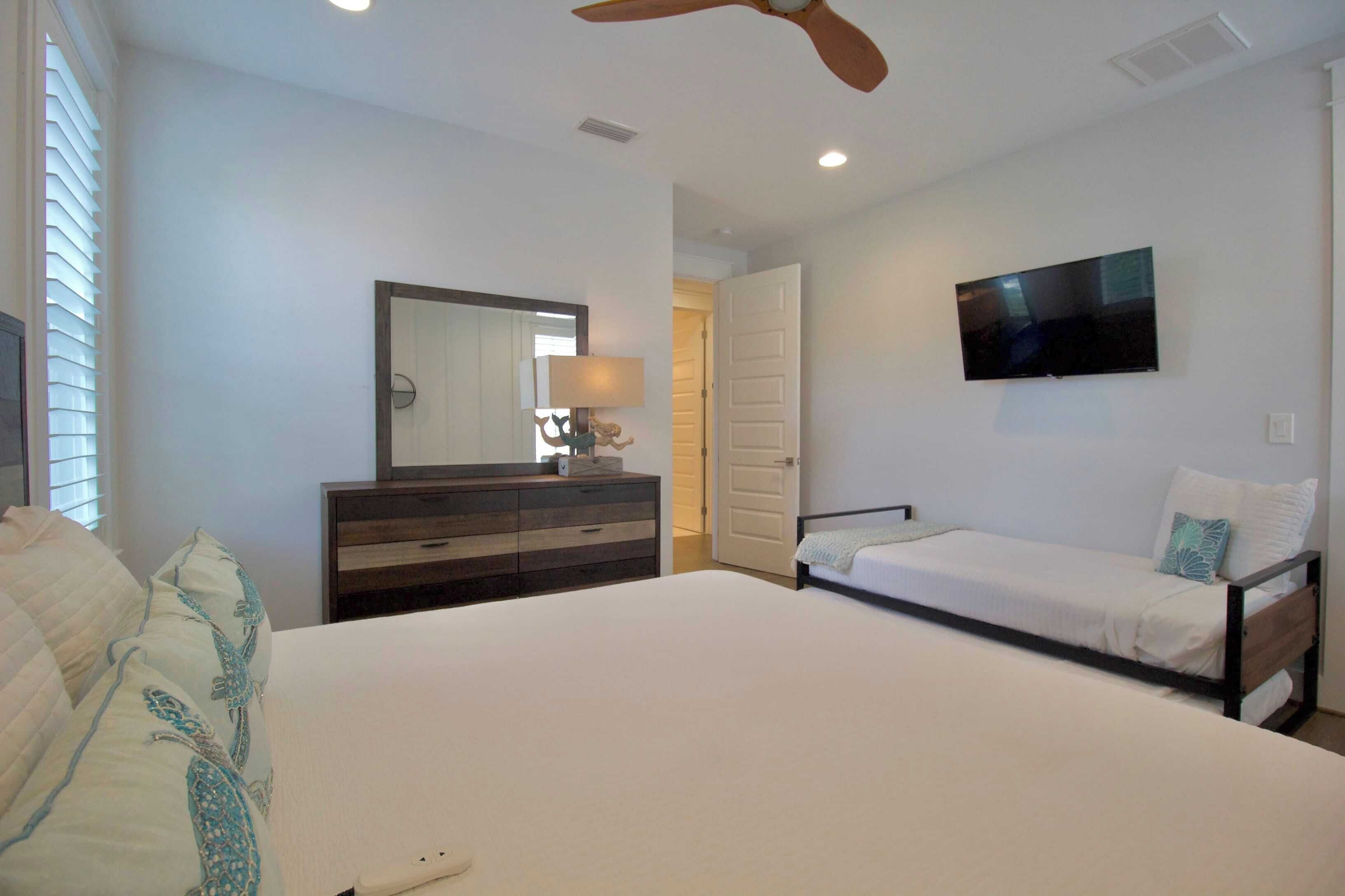 Une chambre à coucher comprenant un lit, une commode, un téléviseur et un ventilateur de plafond.