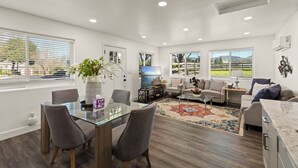 Una sala de estar moderna con una mesa de comedor de vidrio, asientos cómodos, un ventanal con vistas y una alfombra decorativa.