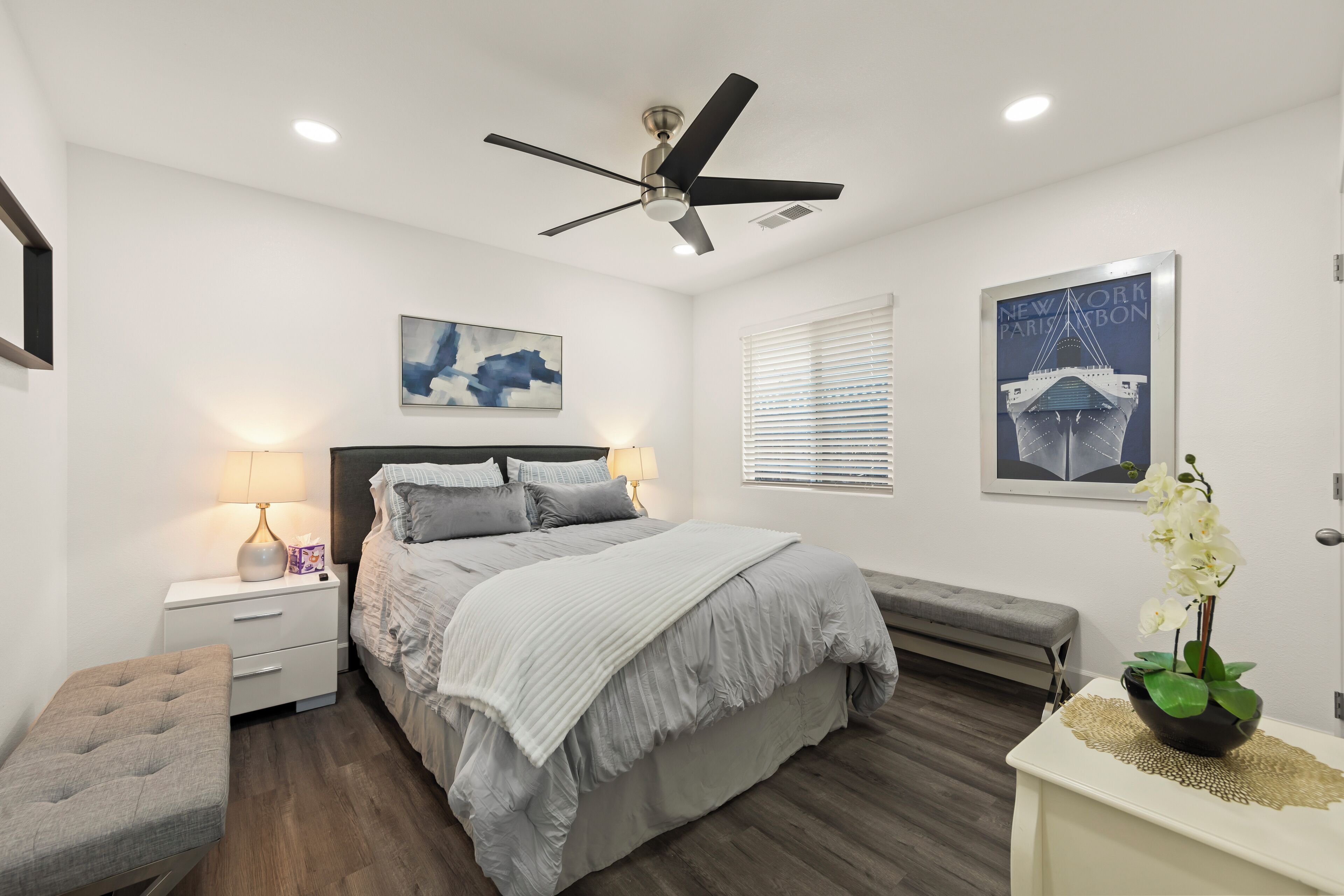 Une chambre à coucher comprenant un lit, une table de chevet, une lampe, un banc et un ventilateur de plafond.