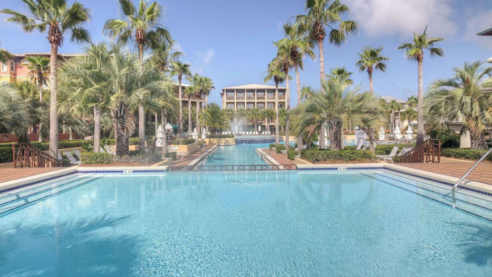 A swimming pool with lounge chairs and palm trees, surrounded by hotel buildings.