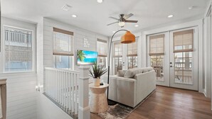 A modern living room with a sofa, a television, and a ceiling fan. - Steps to Beach Pool, Bikes & Game Room Seacrest 5BR (Panama City Beach)
