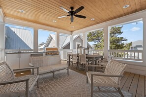 Eine überdachte Terrasse im Freien mit Korbmöbeln, einem Grill und einem Deckenventilator.