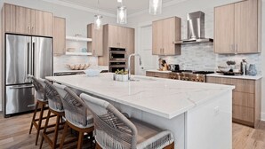 A modern kitchen with a large island, stainless steel appliances, wooden cabinets, and pendant lighting. - Steps to Beach Pool, Bikes & Game Room Seacrest 5BR (Panama City Beach)