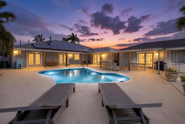 A pool area with lounge chairs, a swimming pool, and a building with multiple windows and doors.