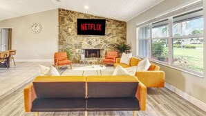 Ein modernes Wohnzimmer mit Kamin aus Stein, orangefarbenen Sofas und einem großen Fenster mit Blick ins Freie.