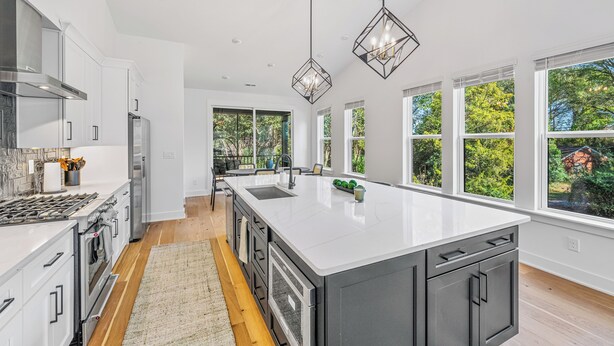 A modern kitchen with a large island, stainless steel appliances, and large windows offering views of greenery.