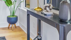 A modern interior with a large window, a black console table, a potted plant, a gold lamp, and a decorative vase.
