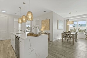 Cozinha moderna com ilha de mármore, luminárias pendentes e área de jantar com vista.