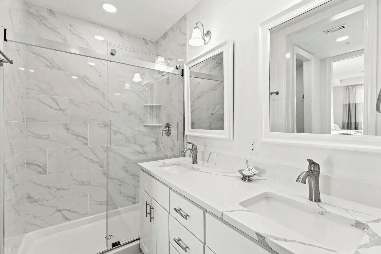 A modern bathroom with marble tiles, a glass shower enclosure, a double sink vanity, and a large mirror.