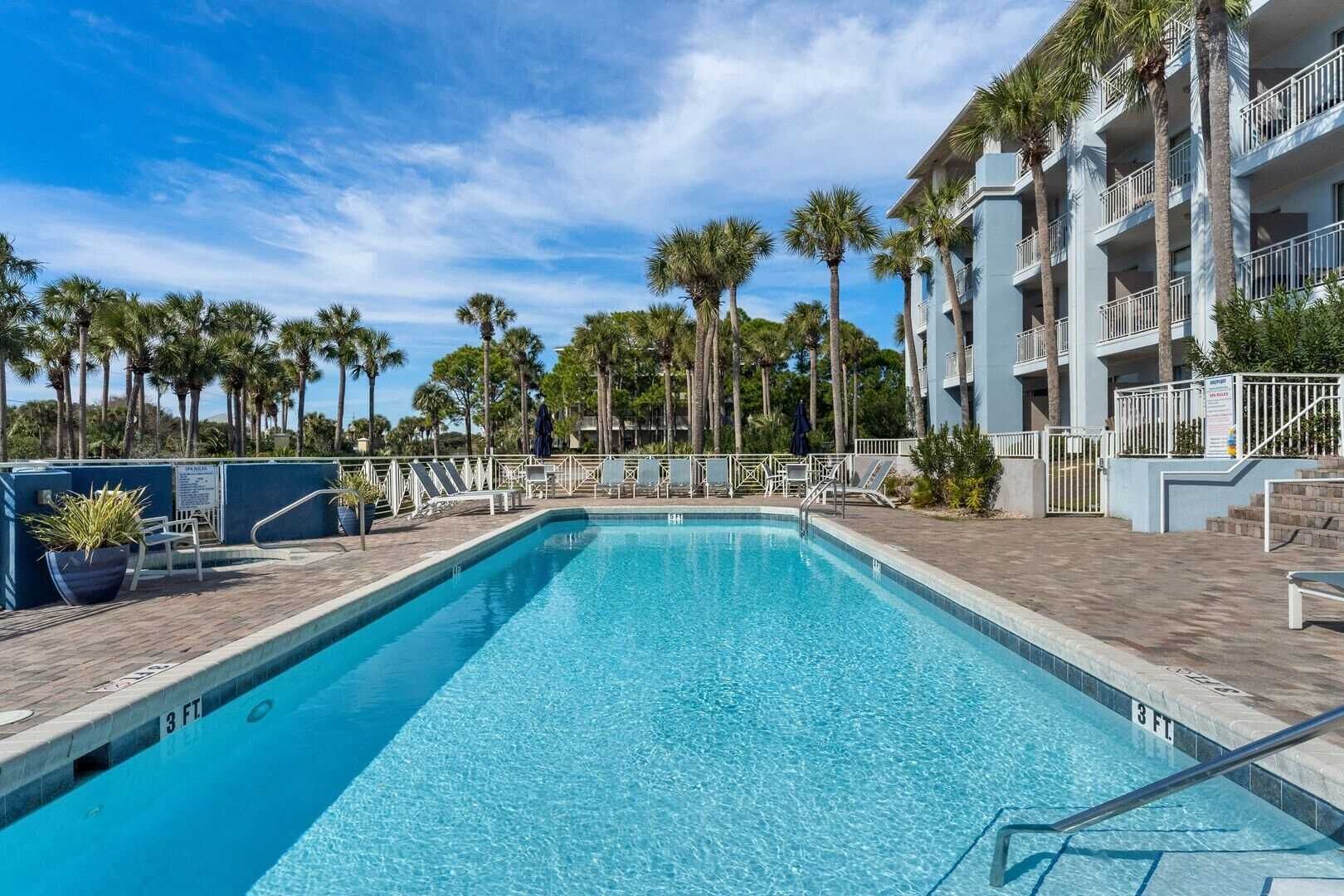 A rectangular swimming pool with a 3 FT depth marking, surrounded by lounge chairs and palm trees, with a multi-story building in the background.