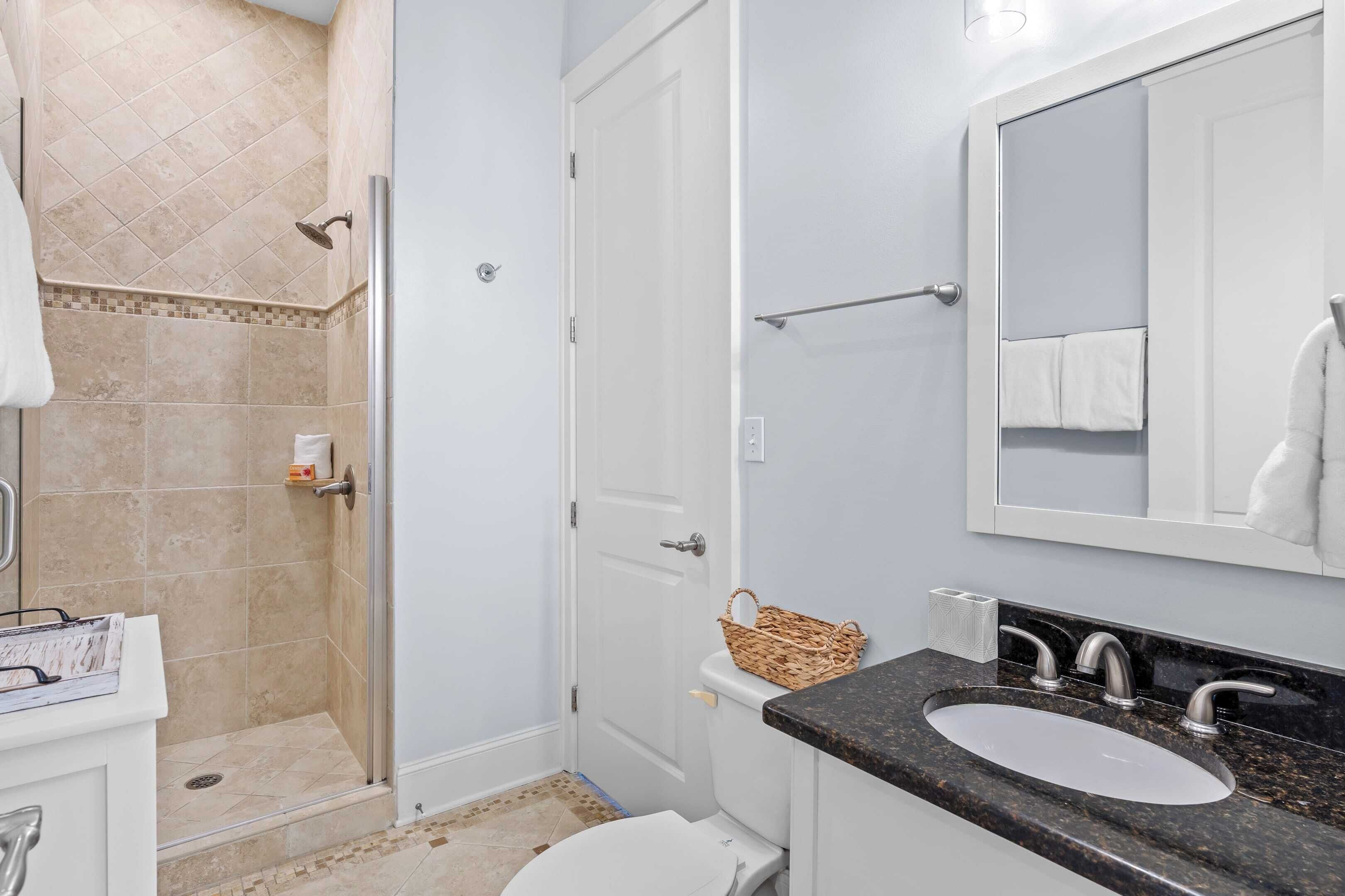 A bathroom with a shower, toilet, sink, and a large mirror.