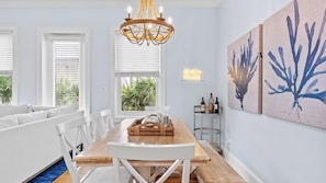 A dining area with a wooden table, white chairs, a chandelier, and artwork on the wall. - Emerald Paradise 2 Blocks to Beach Rooftop Patio + Pool Access Sleeps 10 (Santa Rosa Beach)