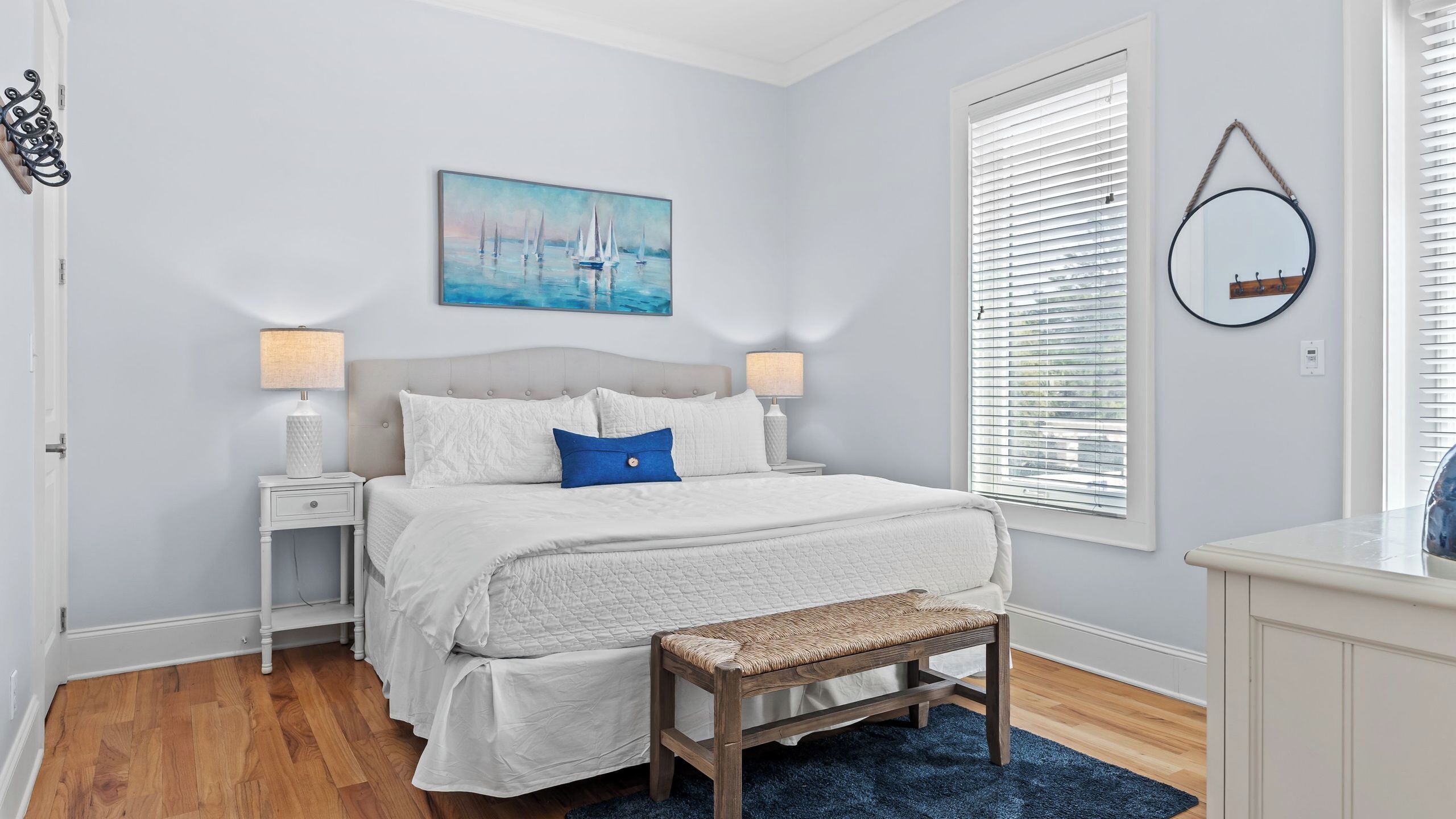 A bedroom with a bed, bedside tables, a bench, a painting, and a window with blinds.